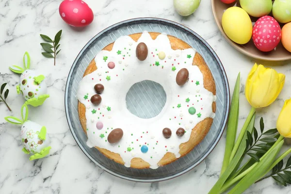 Lezzetli Paskalya pastası, boyanmış yumurtalar, sarı laleler ve yeşil yapraklar beyaz ahşap masada, düz yatıyordu.