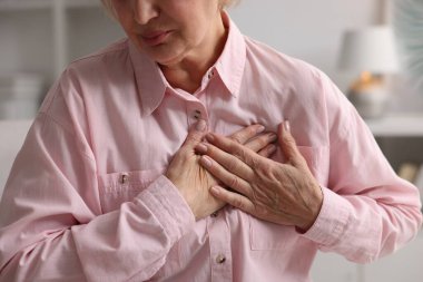 Kalp krizi geçirdi. Üst düzey kadın göğüs ağrısı çekiyor. Kapalı bir yerde, yakın plan.