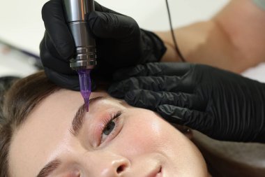 Güzellik uzmanı genç bayana kalıcı kaş makyajı yapıyor.