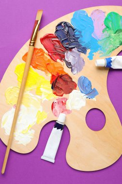 Suluboya boyalı palet, tüpler ve mor arka planda fırça, düz uzanma