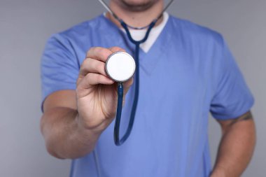 Gri arkaplan ve seçici odaklı steteskop kullanan bir tıp çalışanı.