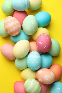 Many painted Easter eggs on yellow background, flat lay