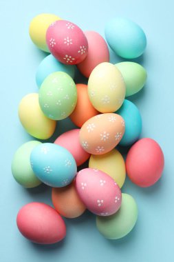 Many painted Easter eggs on light blue background, flat lay