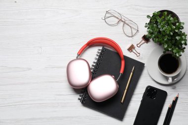 Kulaklıklar, akıllı telefon, kahve, bardaklar, kırtasiye ve çiçek dekoru beyaz ahşap masa, düz yatak. Metin için boşluk