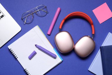 Kulaklıklar, dizüstü bilgisayarlar, gözlükler ve mavi arka planda kırtasiye malzemesi, düz konum
