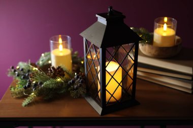 Noel feneri, yanan mumlar, ahşap masa üzerindeki kitap ve dekor koyu pembe arka plan, yakın plan.