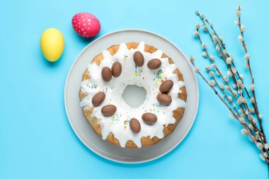 Lezzetli Paskalya pastası, söğüt dalları ve açık mavi arka planda boyanmış yumurtalar, düz uzanmış.