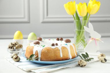 Sarı laleli Paskalya pastası, tavşan figürü, bıldırcın ve beyaz masaya boyanmış yumurta, yakın plan.