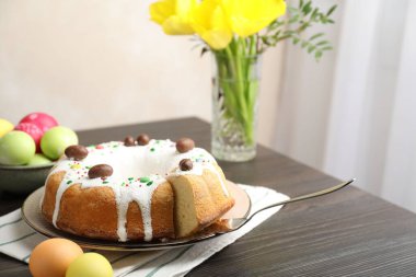 Lezzetli Paskalya pastası. Kapalı masa üzerinde boyalı yumurtalar, sunucu ve sarı laleler. Yakın plan.