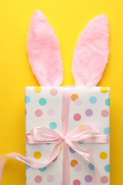 Mutlu Paskalyalar. Sarı arka planda tavşan kulaklığı ve hediye, üst manzara.