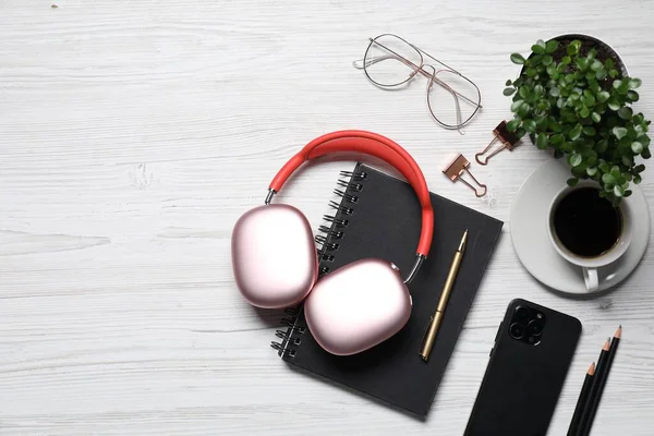 Kulaklıklar, akıllı telefon, kahve, bardaklar, kırtasiye ve çiçek dekoru beyaz ahşap masa, düz yatak. Metin için boşluk