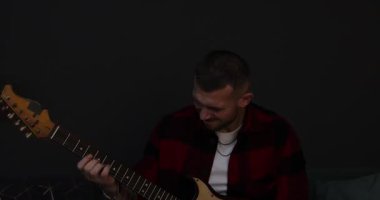 Elektro gitar çalan ve kapalı alanda renkli ışıklarla şarkı söyleyen bir adam. Kamera aşağı iniyor