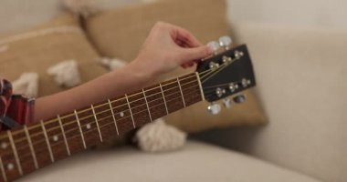 Gitarı akort eden ve evdeki kanepede çalan kadın, yakın çekim.