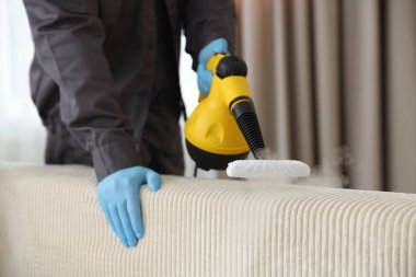 Haşere kontrol görevlisi kanepeyi temizliyor, kapalı alanda buharlı temizleyici ile, yakın plan. Metin için boşluk