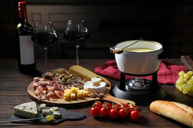 Nefis eritilmiş peynir fondü kabında, abur cubur ve şarap ahşap masada, karanlık arka planda, yakın planda.