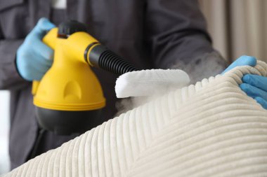 Haşere kontrol işçisi kanepeyi temizliyor. Kapalı alanda buhar temizleyicisi var.