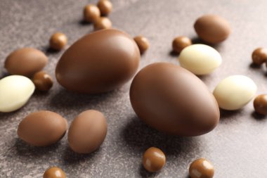 Paskalya kutlaması. Gri desenli masada bir sürü çikolata yumurtası ve dragee, yakın plan.