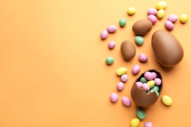 Soluk turuncu arka planda çikolatalı Paskalya yumurtaları ve şekerler. Metin için boşluk