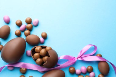 Çikolatalı Paskalya yumurtaları ve açık mavi arka planda menekşe kurdelesi. Metin için boşluk