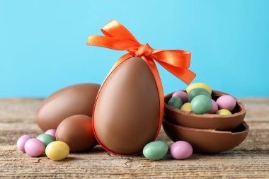 Ahşap masanın üzerinde renkli şekerlemeli lezzetli çikolata yumurtaları açık mavi arka planda, yakın plan. Mutlu Paskalyalar