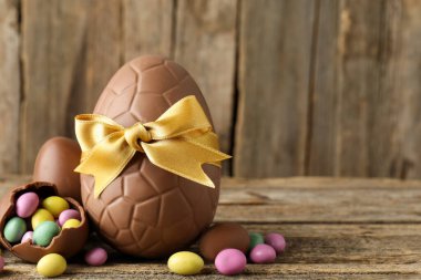 Mutlu Paskalyalar. Ahşap masada renkli şekerlemeli lezzetli çikolata yumurtaları, yakın plan. Metin için boşluk