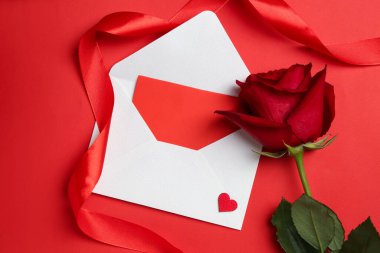 Zarfta aşk mektubu ve kırmızı arka planda gül, düz yatıyordu.
