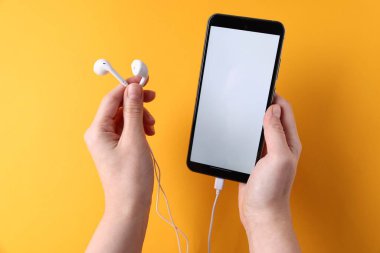 Sarı arka planda akıllı telefonu ve kulaklığı olan bir kadın.