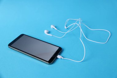 Açık mavi arka planda kulaklıklı akıllı telefon, yakın plan.