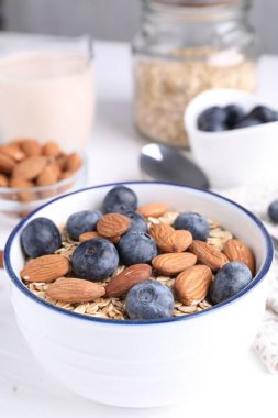 Yulaf gevreği, yaban mersini, fındık ve badem sütü, beyaz masada, yakın plan.
