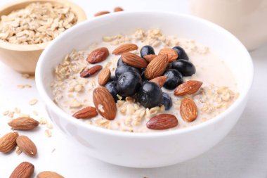 Badem sütlü yulaf gevreği, fındık ve yaban mersini beyaz masada, yakın plan.