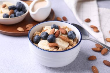 Bademli yulaf gevreği, yaban mersini, muz ve süt açık gri masada, yakın plan.