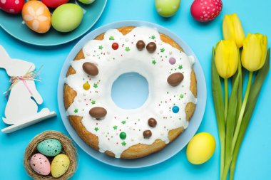 Lezzetli Paskalya pastası, boyanmış yumurtalar, güzel laleler ve açık mavi arka planda dekoratif tavşanlar.