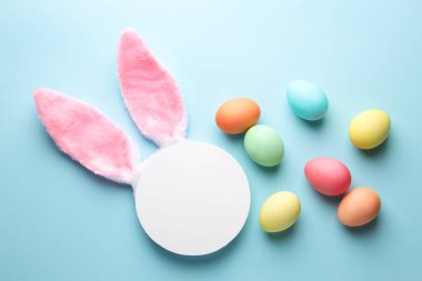 Mutlu Paskalyalar. Şirin tavşan kulakları, boş podyum ve açık mavi arka planda boyanmış yumurtalar, düz uzanmış.