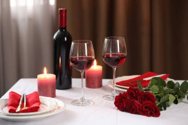 Şarap kadehleri, yanan mumlar ve kırmızı güllerle dolu güzel bir masa.