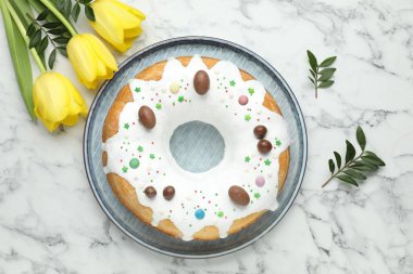 Lezzetli Paskalya pastası, sarı laleler ve yeşil yapraklar beyaz mermer masada, düz uzanmış