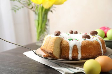 Lezzetli Paskalya pastası. Kapalı masa üzerinde boyalı yumurtalar, sunucu ve sarı laleler. Yakın plan.