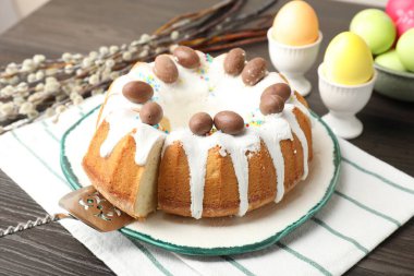 Lezzetli Paskalya pastası, boyalı yumurtalar, sunucu ve söğüt dalları ahşap masada, yakın plan.