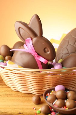 Çikolatalı Paskalya tavşanı hasır sepetin içinde yumurta ve şekerle ahşap masada, yakın plan.