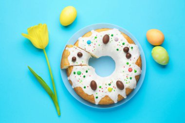 Lezzetli Paskalya pastası, boyanmış yumurtalar ve açık mavi arka planda sarı lale, düz uzanmış.