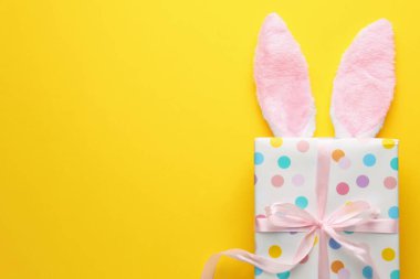 Mutlu Paskalyalar. Tavşan kulaklığı ve sarı arka planda hediye, üst manzara. Metin için boşluk