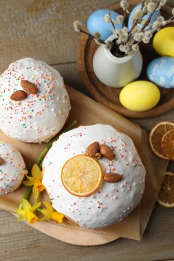 Lezzetli Paskalya pastaları, boyanmış yumurtalar ve söğüt dalları ahşap masada, düz uzanmış.