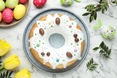 Lezzetli Paskalya pastası, boyanmış yumurtalar, sarı laleler ve yeşil yapraklar beyaz ahşap masada, düz yatıyordu.