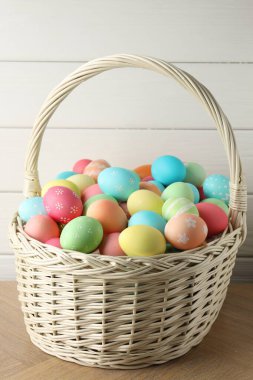 Güzel dekore edilmiş Paskalya yumurtaları hasır sepetin içinde ahşap masanın üzerinde, yakın plan.