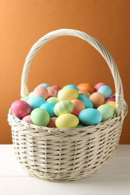 Güzel dekore edilmiş Paskalya yumurtaları hasır sepetin içinde beyaz ahşap masada kahverengi arka planda, yakın planda.