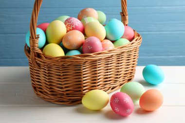 Güzel dekore edilmiş Paskalya yumurtaları hasır sepetin içinde beyaz ahşap masanın üzerinde, yakın plan.