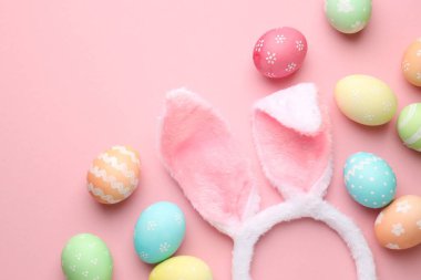 Mutlu Paskalyalar. Tavşan kulaklı şirin saç bandı ve pembe arka planda yumurta boyası, düz yatak. Metin için boşluk