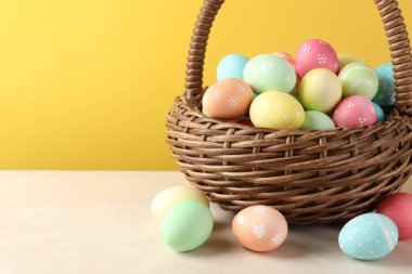 Beyaz masadaki sepetteki güzel Paskalya yumurtaları sarı arka planda, yakın plan. Metin için boşluk