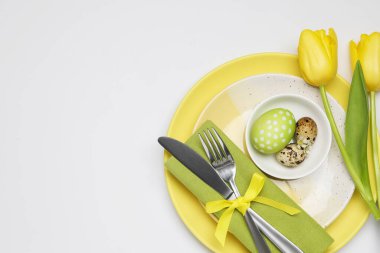 Paskalya kutlaması. Beyaz arka planda lale çiçekleri, boyanmış bıldırcın yumurtaları ve üst manzaralı şenlik masası. Metin için boşluk