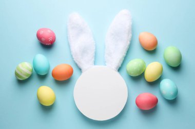 Mutlu Paskalyalar. Şirin tavşan kulakları, boş podyum ve açık mavi arka planda boyanmış yumurtalar, düz uzanmış.