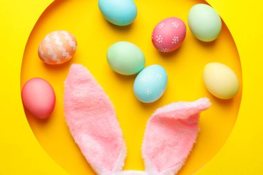 Mutlu Paskalyalar. Sevimli tavşan kulakları ve sarı arka planda deliğe boyanmış yumurtalar.